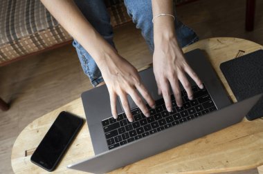 Kadın kanepede oturuyor ve ahşap masada dizüstü bilgisayar kullanıyor. İnternette çalış ve çalış, serbest çalış. Serbest meslek sahibi bir kız defteriyle çalışıyor. Masasında telefon ve okuyucusuyla bir kanepede oturuyor..