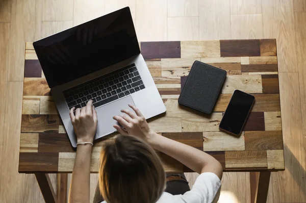 Mujeres manos escribiendo en la vista superior del teclado portátil. Estudiar y trabajar en línea, freelance. Mujer por cuenta propia o independiente, chica que trabaja con su portátil sentado en la mesa de madera con un teléfono y un lector . — Foto de Stock