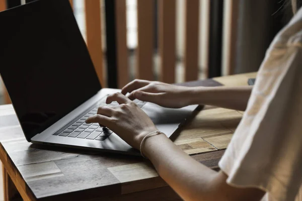 Mujeres manos escribiendo en el teclado del ordenador portátil. Estudiar y trabajar en línea, freelance. Mujer autónoma o independiente, chica que trabaja con su portátil sentado en la mesa de madera con un teléfono, smartphone y lector . — Foto de Stock