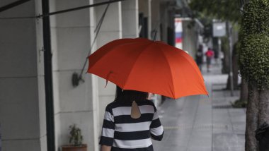 Sokakta yürüyen turuncu şemsiyeli bir kadın..