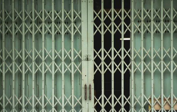 Folding old green metal door gate. Expanded metal sliding gate. Old style grunge metal door. Rustic expanded metal shutter door close with lock pad.