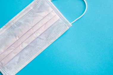 Mavi arka planda pembe tıbbi maske kullanılmış. Koronavirüsü önlemek için ağzı ve burnu kapamak için 3 katlı tıbbi maske. Coronavirus karantinası. Covid-19 'u korumak için antivirüs tıbbi maskesi.