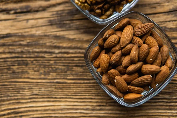 Badem ve ceviz, tahta bir masanın üzerinde duran küçük bir tabakta. Fındık sağlıklı bir vejetaryen protein ve besleyici yemektir. Taşralı eski odunlarda fındıklar.