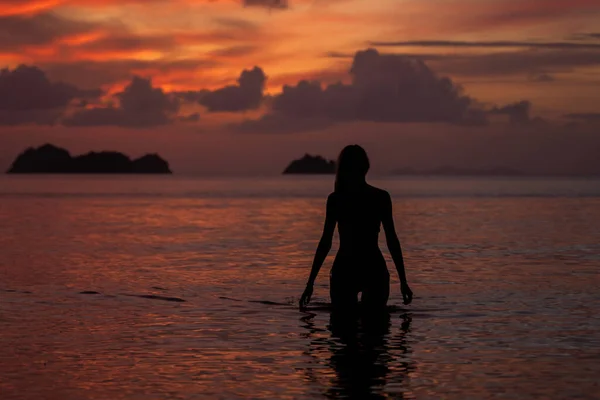 Silhueta de uma mulher na água do mar ou do oceano ao pôr do sol . — Fotografia de Stock