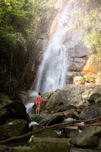 Belle jeune femme blonde mince aux cheveux bouclés, portant en maillot de bain rouge est profiter dans le lagon d'une énorme cascade tropicale dans la jungle. Concept de voyage. Femme sexy portant un maillot de bain rouge dans la jungle . — Photo