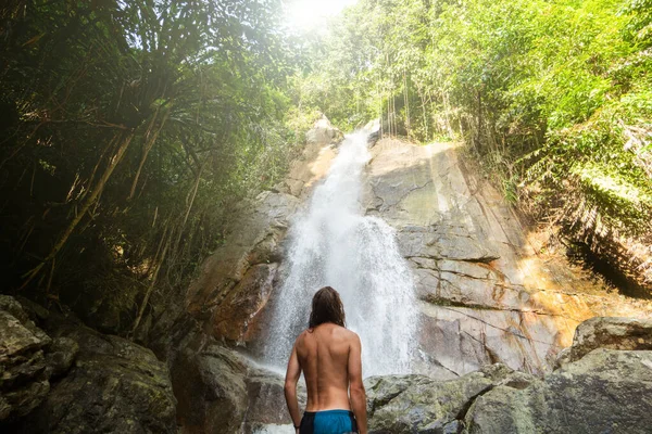 Homme aux cheveux longs est profiter dans la lagune d'une énorme cascade tropicale dans la jungle. Concept de voyage . — Photo