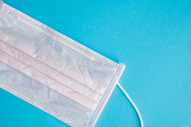 Mavi arka planda pembe tıbbi maske kullanılmış. Koronavirüsü önlemek için ağzı ve burnu kapamak için 3 katlı tıbbi maske. Coronavirus karantinası. Covid-19 'u korumak için antivirüs tıbbi maskesi.