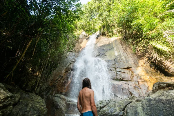 Homme aux cheveux longs est profiter dans la lagune d'une énorme cascade tropicale dans la jungle. Concept de voyage . — Photo