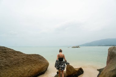 Sahilde elinde taşlarla dikilen ve ufukta görünen bir kadın..