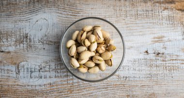 Eski ahşap bir masada küçük bir tabakta şam fıstığı. Pistachio sağlıklı bir vejetaryen protein yiyeceğidir. Doğal çerezler.