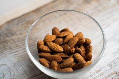 Bademler eski ahşap bir masada küçük bir tabakta. Badem sağlıklı bir vejetaryen protein yiyeceğidir. Doğal çerezler.