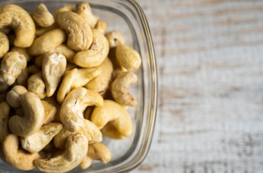 Arka plan olarak eski ahşap bir masada küçük bir tabakta kaju fıstığı. Kaju fıstığı sağlıklı bir vejetaryen protein yiyeceğidir..