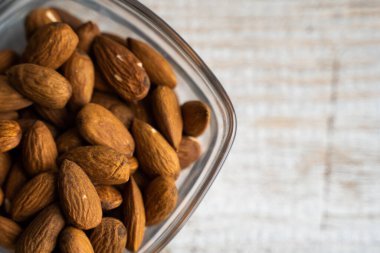 Bademler eski ahşap bir masada küçük bir tabakta. Badem sağlıklı bir vejetaryen protein yiyeceğidir. Doğal çerezler.
