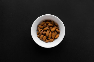 Siyah bir masada küçük bir tabakta badem. Badem sağlıklı bir vejetaryen protein yiyeceğidir. Doğal çerezler.