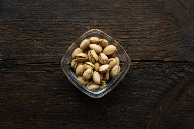 Eski ahşap bir masada küçük bir tabakta şam fıstığı. Pistachio sağlıklı bir vejetaryen protein yiyeceğidir. Doğal çerezler.