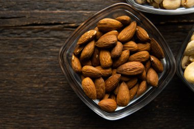Bademler eski ahşap bir masada küçük bir tabakta. Badem sağlıklı bir vejetaryen protein yiyeceğidir. Doğal çerezler.