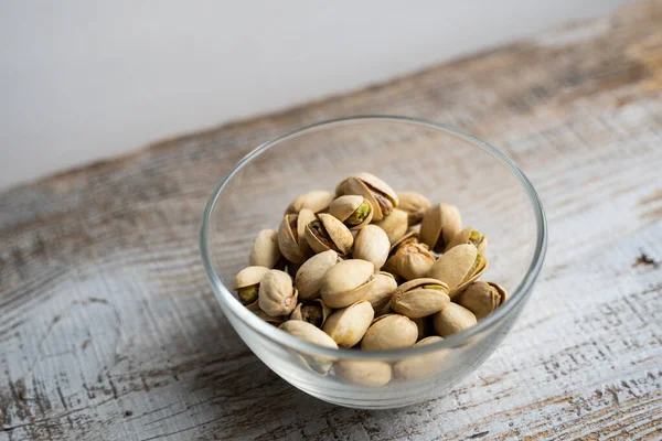 Pistachios in a small plate on a vintage wooden table. Pistachio is a healthy vegetarian protein nutritious food. Natural nuts snacks. — Stock Photo, Image