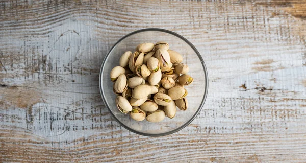 Pistachios in a small plate on a vintage wooden table. Pistachio is a healthy vegetarian protein nutritious food. Natural nuts snacks. — Stock Photo, Image