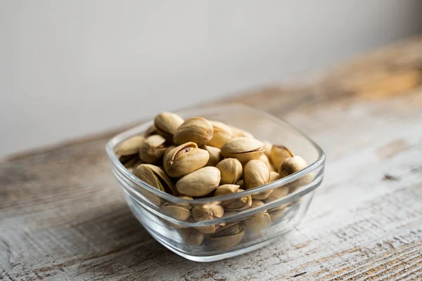 Pistachios in a small plate on a vintage wooden table. Pistachio is a healthy vegetarian protein nutritious food. Natural nuts snacks. — Stock Photo, Image