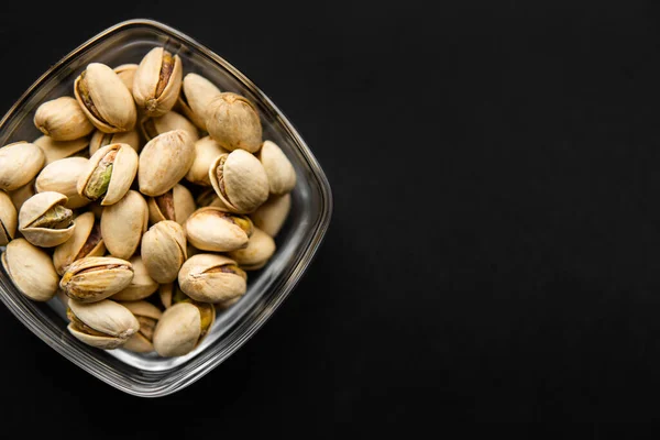 Pistachios in a small plate on a black table. Pistachio is a healthy vegetarian protein nutritious food. Natural nuts snacks. — Stock Photo, Image