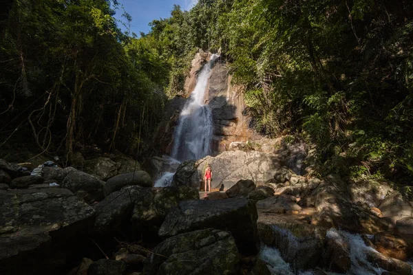 Belle jeune femme blonde mince aux cheveux bouclés, portant en maillot de bain rouge est profiter dans le lagon d'une énorme cascade tropicale dans la jungle. Concept de voyage. Femme sexy portant un maillot de bain rouge dans la jungle . — Photo