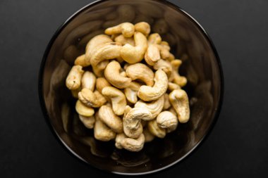 Arka plan olarak siyah bir masada küçük bir tabakta kaju fıstığı. Kaju fıstığı sağlıklı bir vejetaryen protein yiyeceğidir..