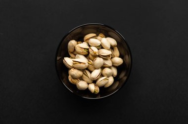 Siyah bir masada küçük bir tabakta şam fıstığı. Pistachio sağlıklı bir vejetaryen protein yiyeceğidir. Doğal çerezler.