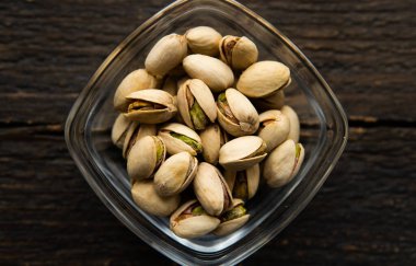 Eski ahşap bir masada küçük bir tabakta şam fıstığı. Pistachio sağlıklı bir vejetaryen protein yiyeceğidir. Doğal çerezler.
