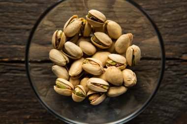 Eski ahşap bir masada küçük bir tabakta şam fıstığı. Pistachio sağlıklı bir vejetaryen protein yiyeceğidir. Doğal çerezler.