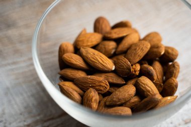 Bademler eski ahşap bir masada küçük bir tabakta. Badem sağlıklı bir vejetaryen protein yiyeceğidir. Doğal çerezler.