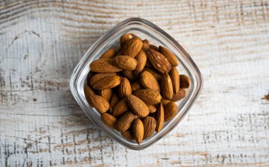 Bademler eski ahşap bir masada küçük bir tabakta. Badem sağlıklı bir vejetaryen protein yiyeceğidir. Doğal çerezler.