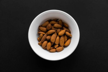 Siyah bir masada küçük bir tabakta badem. Badem sağlıklı bir vejetaryen protein yiyeceğidir. Doğal çerezler.
