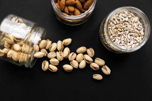 stock image Pistachio scattered on the black table from a jar. Walnut is a healthy vegetarian protein nutritious food.