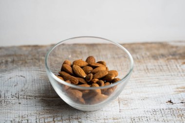 Bademler eski ahşap bir masada küçük bir tabakta. Badem sağlıklı bir vejetaryen protein yiyeceğidir. Doğal çerezler.