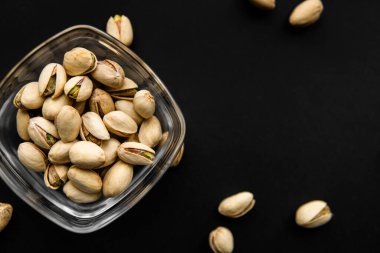 Siyah bir tabağın etrafına saçılmış badem cevizleri olan küçük bir tabakta şam fıstığı. Pistachio sağlıklı bir vejetaryen protein yiyeceğidir. Doğal çerezler.