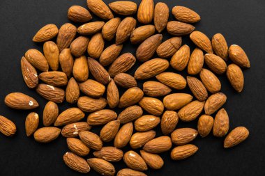 Bademler siyah bir masaya saçılmış. Badem sağlıklı bir vejetaryen protein yiyeceğidir. Doğal çerezler.
