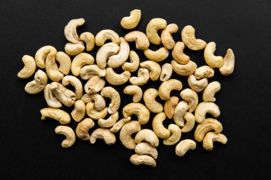 Siyah bir masaya saçılmış kaju fıstığı. Kaju fıstığı sağlıklı bir vejetaryen protein yiyeceğidir..