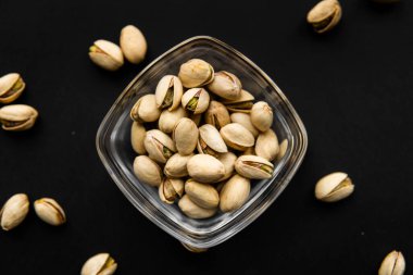 Siyah bir tabağın etrafına saçılmış badem cevizleri olan küçük bir tabakta şam fıstığı. Pistachio sağlıklı bir vejetaryen protein yiyeceğidir. Doğal çerezler.