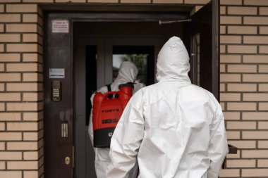 UKRAINE, KYIV - 20 Mayıs 2020: Beyaz koruyucu giysili ve maskeli iki adam bina içinde iç yüzeyleri dezenfekte ederken koronavirüs salgını enfeksiyonu önleme ve kontrol etme amaçlı