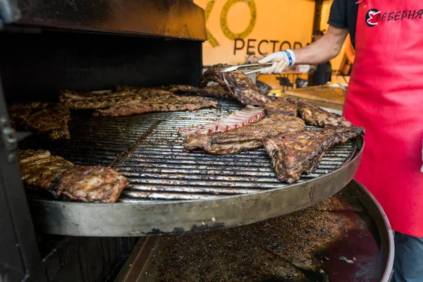 UCRANIA, LUTSK - 5 de junio de 2019: El hombre está cocinando costillas de cerdo en una parrilla en un festival de alimentos . —  Fotos de Stock
