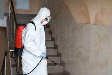 UKRAINE, KYIV - 20 Mayıs 2020: Beyaz koruyucu giysili ve maskeli adam salgının önlenmesi ve kontrol edilmesi için koronavirüs salgını sırasında iç yüzeyleri sterilize ediyor..