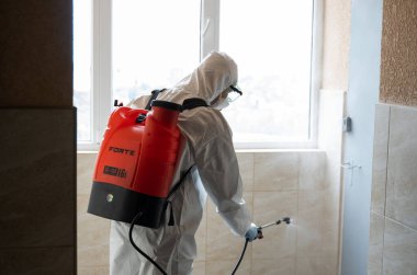 UKRAINE, KYIV - 20 Mayıs 2020: Beyaz koruyucu giysili ve maskeli adam salgının önlenmesi ve kontrol edilmesi için koronavirüs salgını sırasında iç yüzeyleri sterilize ediyor..