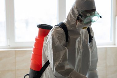 UKRAINE, KYIV - 20 Mayıs 2020: Beyaz koruyucu giysili ve maskeli adam salgının önlenmesi ve kontrol edilmesi için koronavirüs salgını sırasında iç yüzeyleri sterilize ediyor..