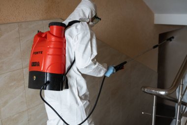UKRAINE, KYIV - 20 Mayıs 2020: Beyaz koruyucu giysili ve maskeli adam salgının önlenmesi ve kontrol edilmesi için koronavirüs salgını sırasında iç yüzeyleri sterilize ediyor..