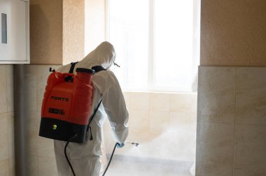UKRAINE, KYIV - 20 Mayıs 2020: Beyaz koruyucu giysili ve maskeli adam salgının önlenmesi ve kontrol edilmesi için koronavirüs salgını sırasında iç yüzeyleri sterilize ediyor..