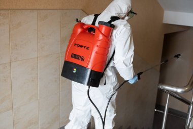 UKRAINE, KYIV - 20 Mayıs 2020: Beyaz koruyucu giysili ve maskeli adam salgının önlenmesi ve kontrol edilmesi için koronavirüs salgını sırasında iç yüzeyleri sterilize ediyor..