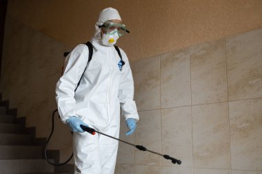 UKRAINE, KYIV - 20 Mayıs 2020: Beyaz koruyucu giysili ve maskeli adam salgının önlenmesi ve kontrol edilmesi için koronavirüs salgını sırasında iç yüzeyleri sterilize ediyor..