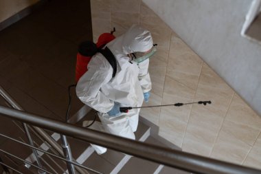 UKRAINE, KYIV - 20 Mayıs 2020: Beyaz koruyucu giysili ve maskeli adam salgının önlenmesi ve kontrol edilmesi için koronavirüs salgını sırasında iç yüzeyleri sterilize ediyor..