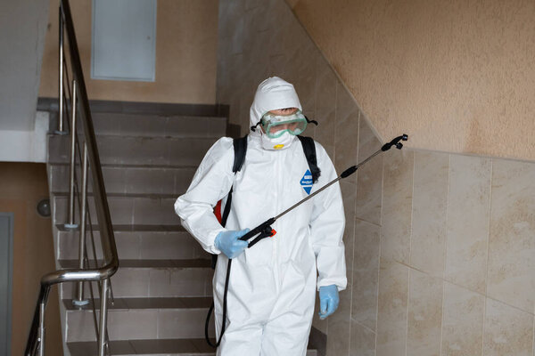 UKRAINE, KYIV - May 20, 2020: Man in a white protective suit and mask is disanitizing interior surfaces inside buildings while the coronavirus epidemic for infection prevention and control of epidemic
.