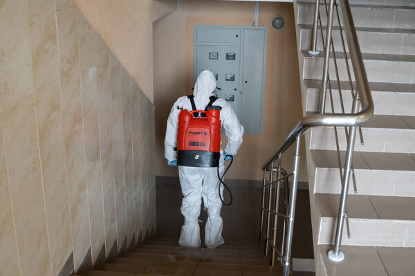 UKRAINE, KYIV - May 20, 2020: Man in a white protective suit and mask is disanitizing interior surfaces inside buildings while the coronavirus epidemic for infection prevention and control of epidemic
.